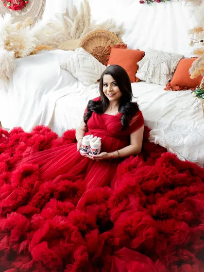 A sweet and joyful portrait. The mom-to-be sits in a sea of red tulle, holding up a pair of "I love Mom/Dad" baby booties.