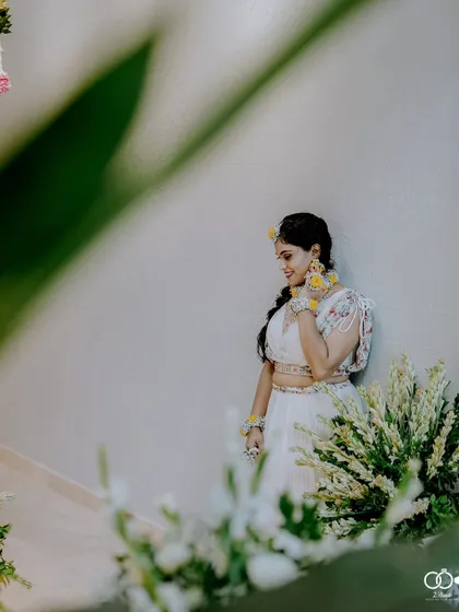 A beautiful, candid portrait of the bride in her white Haldi lehenga, framed by flowers.