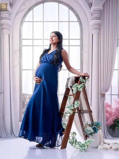 A royal blue gown stands out against a grand, window-themed studio backdrop, creating a regal and sophisticated portrait.