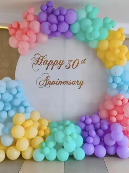 A soft and cheerful 30th anniversary celebration, featuring a circular backdrop framed with a rainbow of pastel balloons.