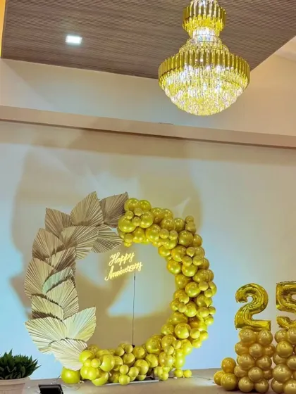 An elegant 25th-anniversary decoration. The all-gold theme features a balloon ring, dried palm leaves, a neon "Happy Anniversary" sign, and large "25" number balloons.