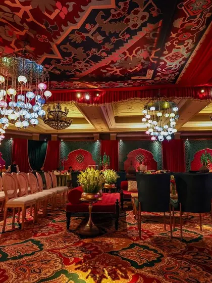 A wide view of the entire hall, showcasing the patterned carpet, the custom ceiling, the multiple lounge areas, and the stage. This image captures the full scope and grandeur of the Sufi Durbar design.