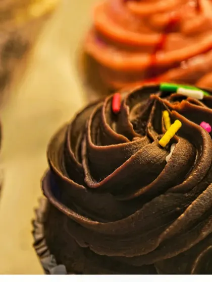 Another angle of the chocolate cupcake, with a strawberry frosted one blurred in the background. This composition adds depth and shows variety, ideal for showcasing a range of bakery offerings.