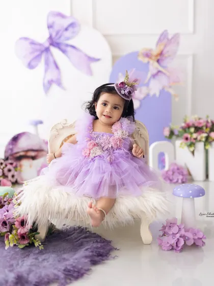 A beautiful portrait of the birthday girl on a miniature vintage chair, part of the purple fairy-themed first birthday celebration.