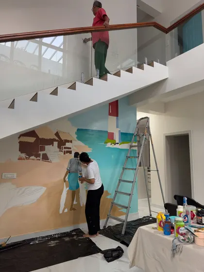 No wall is too tricky, not even a double-height staircase. Here you can see my team and I working on a large beach-themed mural for a client's home, bringing coastal vibes indoors.