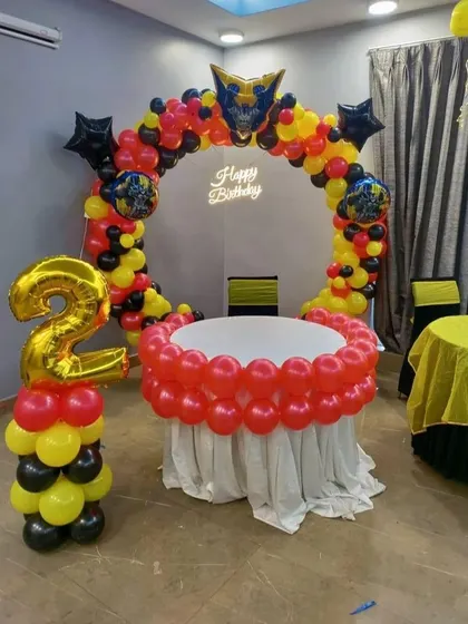 A 'Transformers' or robot-themed second birthday. The balloon arch in red, yellow, and black is topped with a character foil balloon, with a matching number '2' balloon column.