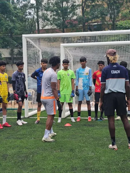 A coach provides direct instruction to a group of aspiring goalkeepers on the training pitch. We emphasize small group coaching to ensure every player gets personalized feedback and guidance.