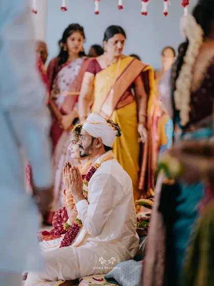 The couple in prayer during their wedding ceremony, surrounded by the warm presence of their family and friends.