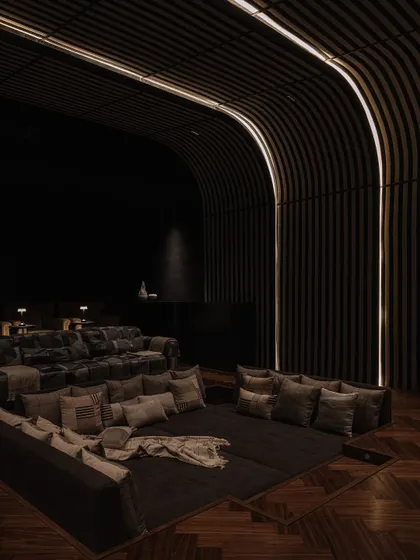 The home theatre features tiered seating with a mix of large sofas and floor cushions, all enveloped by acoustically treated, curved walls. The lighting is designed to be subtle and atmospheric.