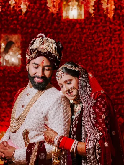 A close, intimate portrait of a couple against a stunning red floral wall. The groom's smile and the bride's gentle lean create a heartwarming image.