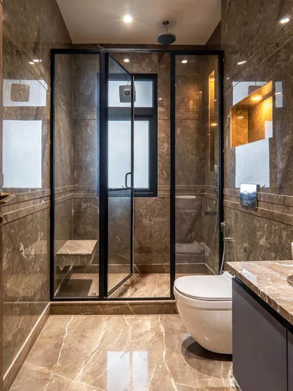 This modern bathroom interior features a glass-enclosed shower with a built-in seat. The entire space is clad in a warm, brown-toned marble, creating a sleek and sophisticated look.