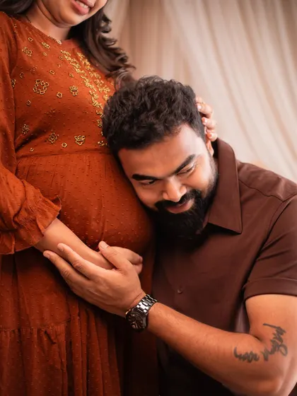 The classic "listening to the bump" pose, captured with beautiful studio lighting that highlights the emotion of the moment.