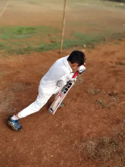 This image perfectly captures a key coaching point: getting your head right on top of the ball. This young batsman demonstrates excellent form while practicing his drive.