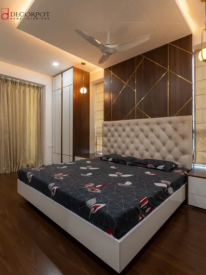 A luxurious master bedroom featuring a floor-to-ceiling tufted headboard and a dark wood accent wall with striking gold inlay. The design is a perfect blend of opulence and modern style.