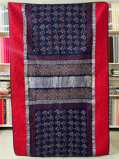 This memory quilt combines the rich navy and red of a traditional saree. The original silver borders are used to frame the intricate patterns, creating a regal and timeless keepsake.