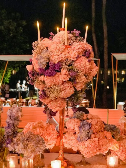 A magnificent centerpiece of pink hydrangeas and roses, with tall taper candles emerging from the blooms. This design adds height and drama to the tablescape, creating a sense of grandeur.