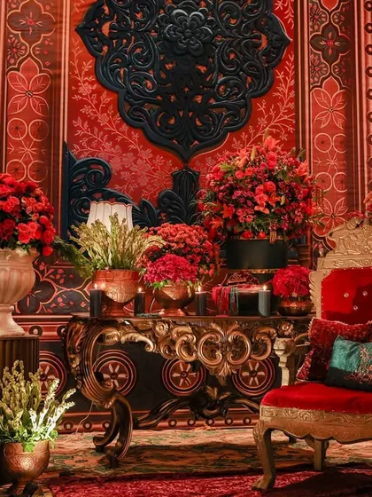 A richly detailed photo corner with an ornate red throne chair and a wall of Indo-Saracenic textures. The space is layered with crimson florals and intricate medallions, inspired by 18th-century Ottoman interiors.