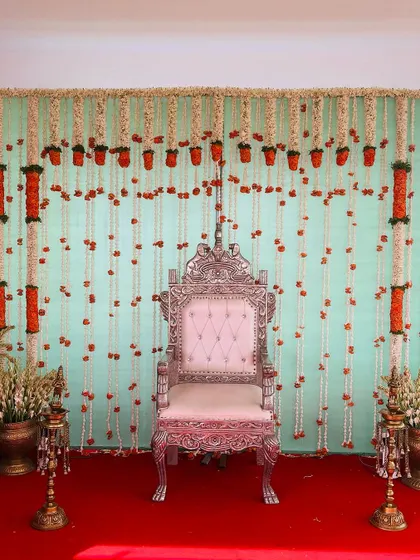 A simple yet beautiful backdrop with hanging strings of jasmine and marigold flowers. The light green curtain and red carpet create a classic and festive color combination.