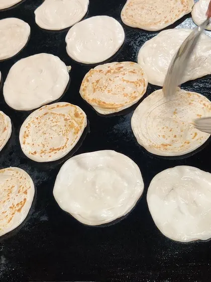 Fresh parathas being cooked on a large tawa. We make our breads live on-site whenever possible to ensure they are served soft and hot, perfect for pairing with our curries.
