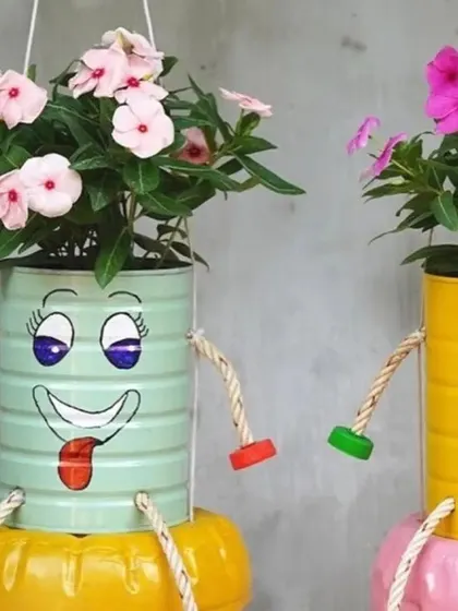 A pair of hanging planters made from painted tin cans. Their dangling legs and cheerful faces add a sense of movement and fun to the garden.