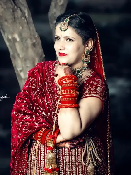 A close-up shot capturing the bride's thoughtful expression and the rich details of her red bangles and velvet dress.