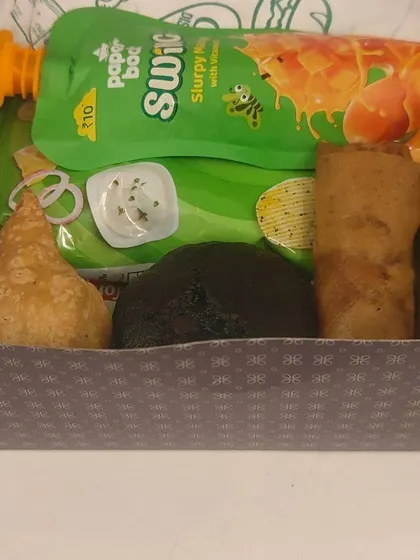 Samosa, spring rolls, a dark muffin and mango drinks fill this snack box we pack with separate items inside.