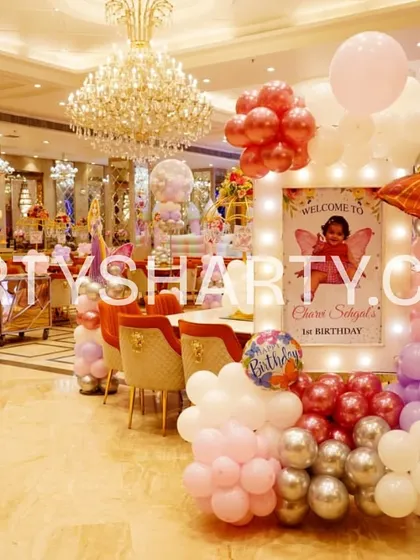 A welcome stand for a butterfly-themed first birthday, featuring a personalized sign, a large butterfly foil balloon, and a cascade of pink, white, and silver balloons.