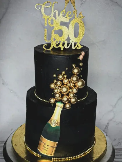 Turning half a century old calls for a celebration, and a cake from me! This two-tiered black and gold 50th birthday cake features a champagne bottle theme with edible golden bubbles.