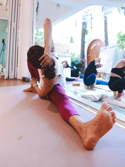 A student moving into a deep expression of Akarna Dhanurasana (Archer Pose), demonstrating incredible hip flexibility and focus. This pose is about daring to try.