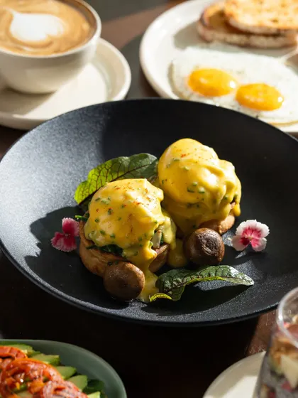 A beautifully plated eggs benedict on a dark plate, which makes the yellow hollandaise sauce stand out.