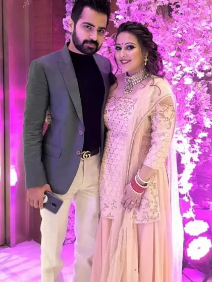 A happy couple at a wedding function. The client is wearing a beautiful peach sharara set by Pooja Peshoria, featuring delicate silver embroidery, perfect for a guest or for pre-wedding festivities.
