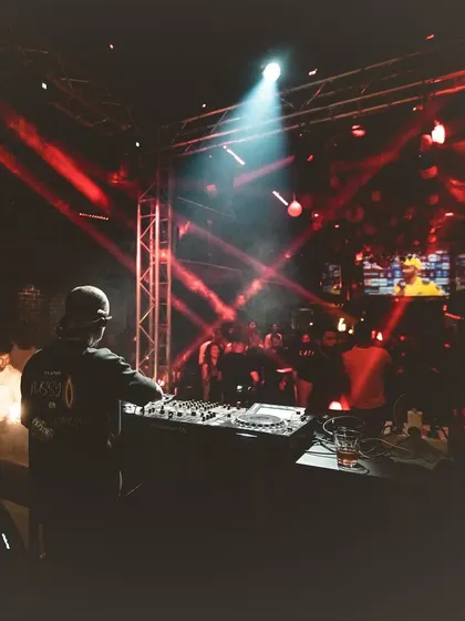 A moody shot from behind the decks, surrounded by red lights and stage rigging.