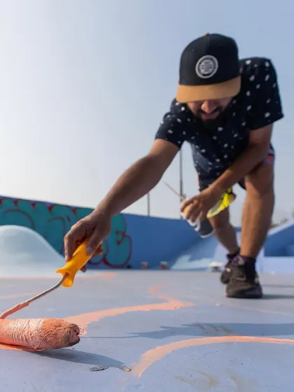 A low-angle shot of me using a roller to lay down the base colors for a large ground mural. The first step is always blocking out the main shapes.