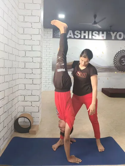 An instructor provides support for a student practicing a handstand against the wall, helping to build the strength and confidence needed for inversions.