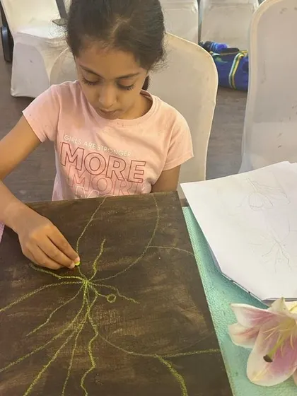 The beginning of a masterpiece. An artist sketches out her floral design on a pre-stained canvas, showing the initial steps of our guided painting sessions.
