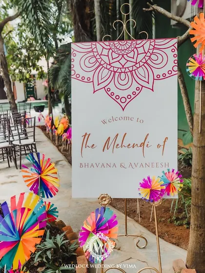 A walkthrough of a carnival-themed Mehendi we designed. The entrance welcomes guests with a custom sign and colorful pinwheels, leading to a festive space filled with bright decor and floral arrangements.