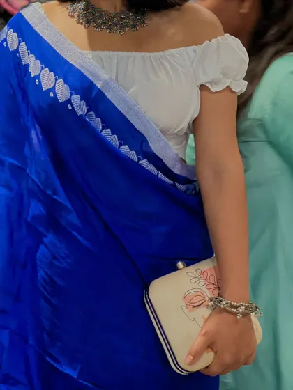 Here you can really see the craftsmanship. The beaded bracelet worn by the customer adds another layer of texture, working in harmony with the clutch and the heart-print border of the saree.