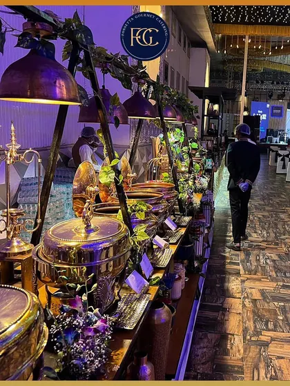 A wide view of an elaborate buffet station at a large event. The setup includes hanging industrial-style lamps and lush greenery, demonstrating our flair for creating immersive, themed dining environments.