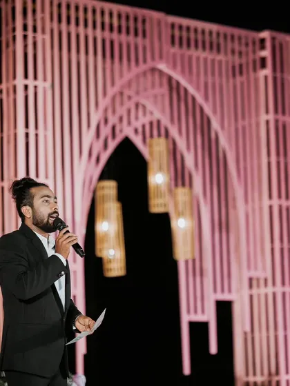 The host addresses the guests during the reception. The modern pink architectural backdrop creates a visually interesting and stylish stage setting.