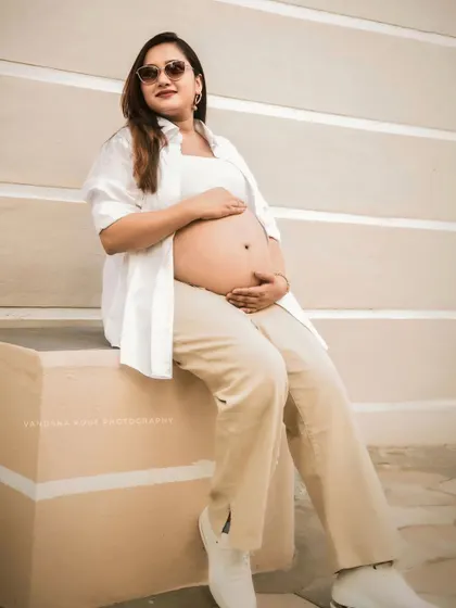 A confident mother-to-be poses in a modern, casual outfit with an open shirt, showcasing her bump in a minimalist outdoor setting.