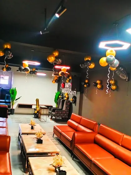 A party setup in a private room with modern decor, accented with black, gold, and silver balloons hanging from the ceiling.