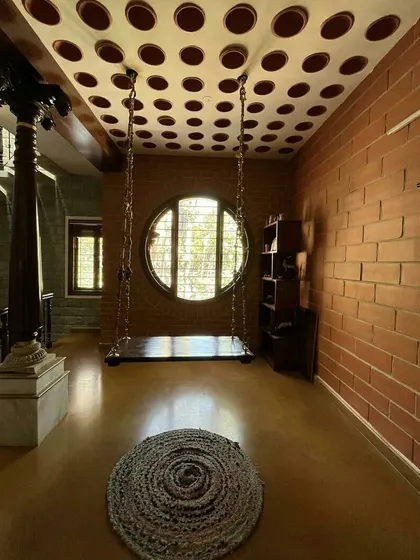 A quiet corner for reflection. This space combines a traditional indoor swing with a modern filler slab ceiling made of clay pots, reducing concrete usage while creating a unique visual texture. The large circular window frames the world outside, making nature a part of the home's interior life.