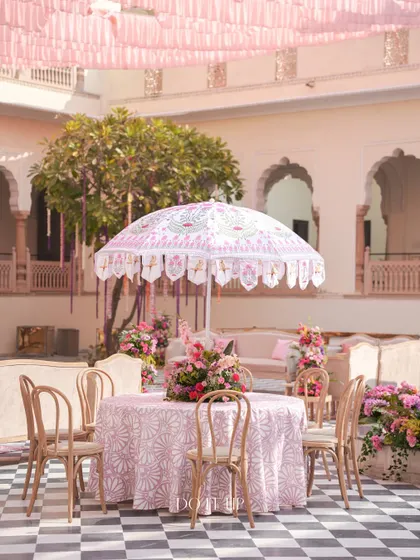 A table at the Jaipur welcome brunch, featuring a custom block-printed tablecloth and a floral centerpiece. The elegant umbrella provides shade and adds a touch of Rajasthani charm.