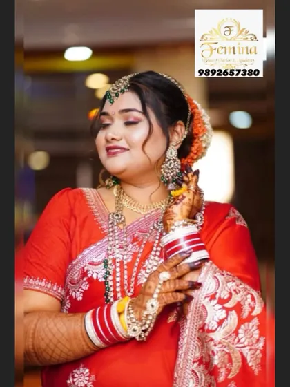 A happy bride in a classic red saree. The makeup is soft and glowing, with defined eyes and a smile that says it all. The hair is styled in a traditional bun with orange flowers.