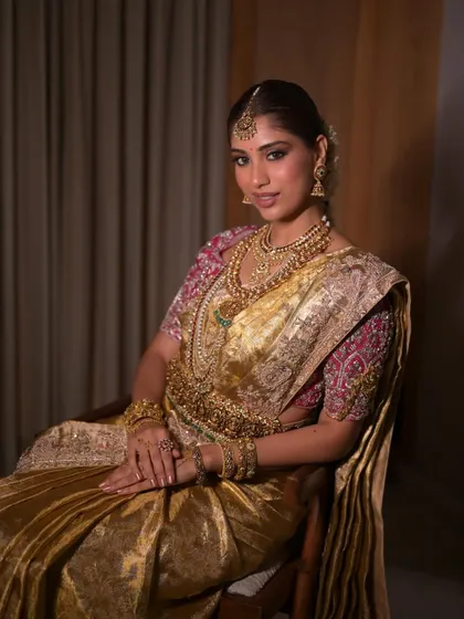 A regal seated portrait of a South Indian bride. The makeup is elegant and understated, allowing the rich texture of the silk saree and the craftsmanship of the jewelry to take center stage.