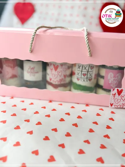 A Valentine's gift bag holding a set of five mini cake tubs, each decorated with a different romantic design like hearts and "XOXO."