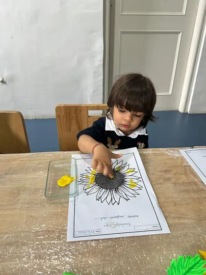 A toddler carefully uses his finger to apply yellow paint to a sunflower template, demonstrating focus and developing his pincer grasp.