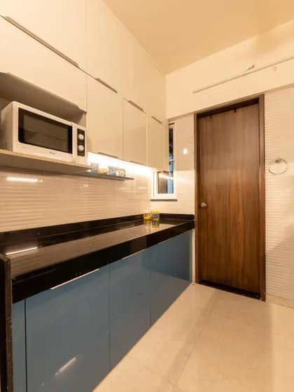 Another angle of the Pune kitchen, showing the seamless integration of the microwave and the clean lines of the handleless modular cabinets, maximizing efficiency in a compact space.
