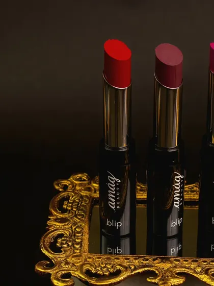 These three lipsticks are presented on an ornate golden tray, creating a look of classic luxury. The dark, moody background makes the vibrant red, mauve, and pink shades appear even richer.