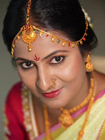 A close-up portrait of a South Indian bride, showing the details of her traditional gold jewelry and bindi.
